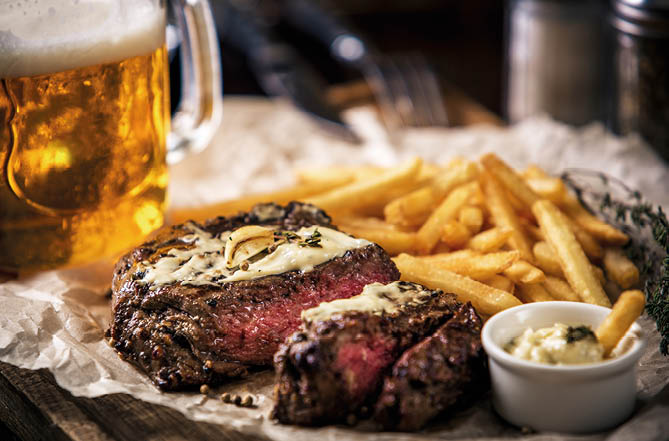 Healthy lean grilled medium-rare steak with french fries, and beer, and a spice in a rustic pub or tavern. Food-styling