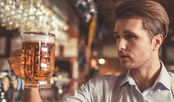 Handsome bartender is examining beer while standing near the bar counter in pub