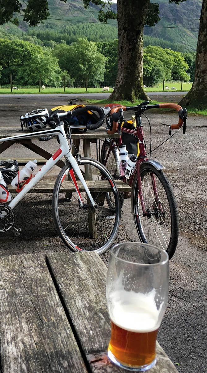 Pair of pints of beer and bikes outside an English county pub in the lake District with benches and lush green fields and trees in the background