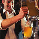 Handsome bartender is smiling and filling a glass with beer while standing at bar counter in pub, close-up